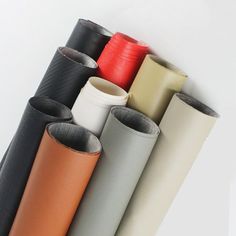 several different colored leathers lined up on a white wall with one red and the other black