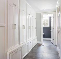 a long hallway with white cabinets and drawers on both sides, leading to an open door