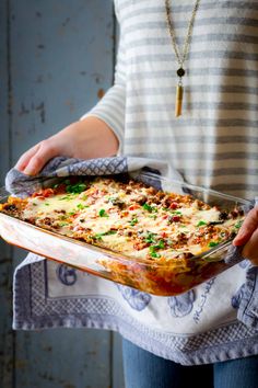 a woman is holding a casserole dish with meat and vegetables on the side