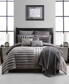 a bed with grey and white striped comforter in a room next to two windows