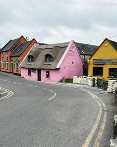 a street with houses painted pink, yellow and green in the background is a winding road