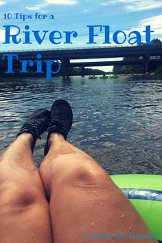 the legs and feet of a person sitting on a raft in water with a bridge in the background