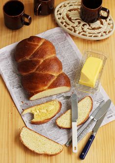 a loaf of bread sitting on top of a cutting board next to butter and two mugs