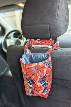 an orange flowered bag hanging from the back seat of a car with its pocket open