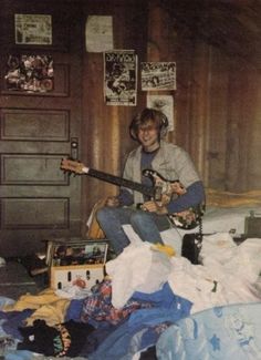 a young man sitting on top of a bed holding an electric guitar in his hand