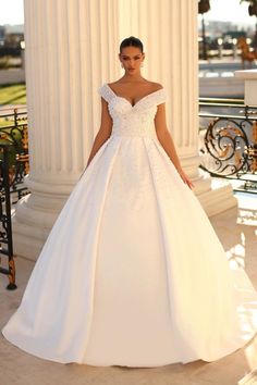 a woman in a white wedding dress standing next to a pillar with her hands on her hips