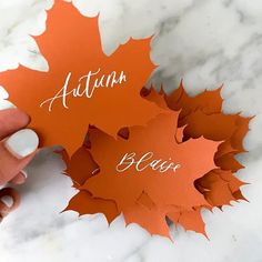 someone is holding an orange leaf with the words autumn and fall below it on a marble surface