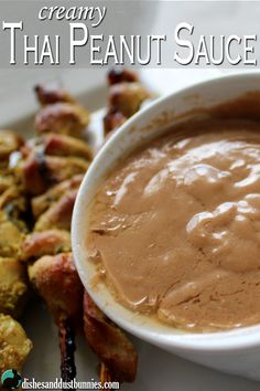 a bowl of peanut sauce next to some chicken skewers on a white plate