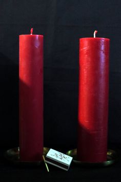 two red candles sitting next to each other on a plate with a small tag in front of them