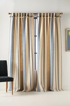 a chair sitting in front of a window with striped curtains