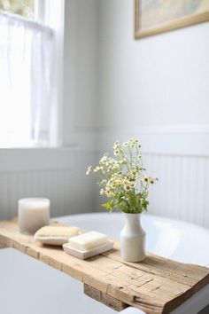 a white vase with flowers sitting on top of a wooden table next to a bath tub