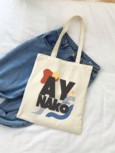 a tote bag sitting on top of a bed next to a pair of jeans