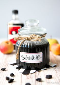 a jar filled with black liquid sitting on top of a wooden table next to an apple