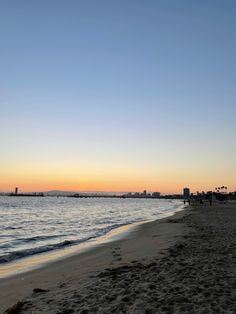 the sun is setting at the beach and people are walking on the sand near the water