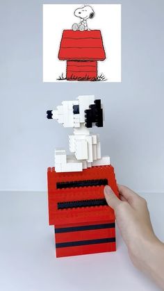 a hand holding a small lego model of a dog on top of a red couch