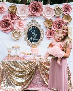 a woman holding a baby in front of a table with pink and gold decorations on it