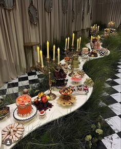 a long table topped with lots of cakes and desserts next to tall candles on top of a black and white checkered floor