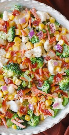 a bowl filled with corn and vegetables on top of a red table cloth next to a fork