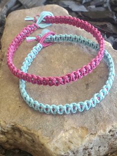 two bracelets sitting on top of a rock next to each other, one is pink and the other is blue