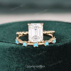 an emerald colored diamond ring on top of a green velvet cushioned box with turquoise stones