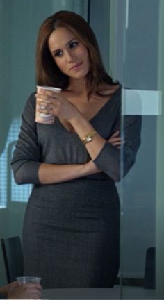 a woman standing in front of a glass wall holding a coffee cup and looking at the camera