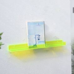 a yellow shelf with a picture on it next to a potted plant and white wall