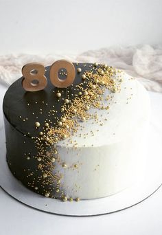 a white cake with gold sprinkles and the number 80 on top is shown