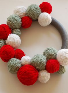 a yarn wreath with red, white and green balls hanging from it's center