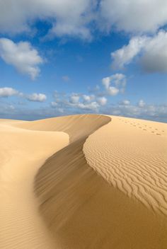 the sky is blue and white with some clouds in it, as well as sand dunes