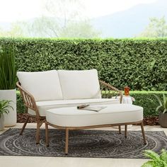 a white couch sitting on top of a rug in front of a green plant covered wall