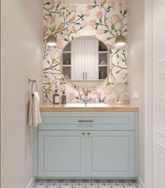 a bathroom with floral wallpaper and light blue cabinetry, along with an oval mirror