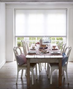 a dining room table set with plates and place settings in front of an open window