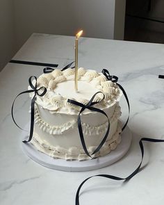 a white cake with a single candle on top and black ribbon around the edges, sitting on a table