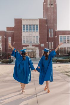 two girls in blue graduation gowns are walking towards the building with their arms up