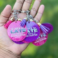 three pink and purple key chains with tassels in the palm of a person's hand