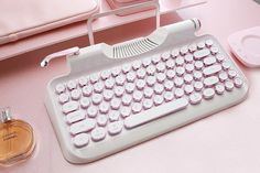 a pink and white desk with a computer keyboard, perfume bottle and bed in the background