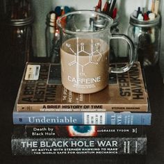 three books stacked on top of each other in front of a glass mug filled with liquid