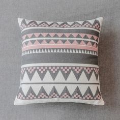 a gray and pink pillow sitting on top of a grey bed next to a wall