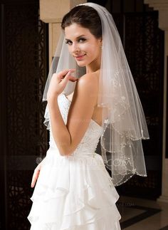 a woman in a wedding dress posing for the camera with her veil over her shoulder