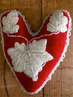 a red and white heart shaped pillow with flowers on it's sides sitting on a wooden surface