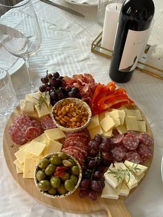 a wooden platter filled with different types of cheese and meats next to wine glasses