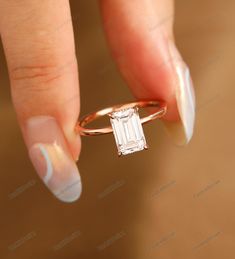 a woman's hand holding a ring with an emerald stone in the middle and white nails