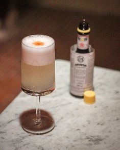 an alcoholic drink sitting on top of a marble table next to a bottle of alcohol