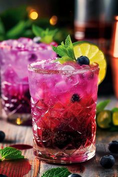 two glasses filled with blueberries and limeade on top of a wooden table next to mint leaves