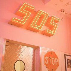 a neon sign that reads stop in front of a pink wall with pictures on it