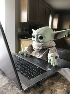 a baby yoda doll sitting on top of a laptop computer