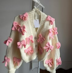 a pink and white sweater with bows hanging on a rack