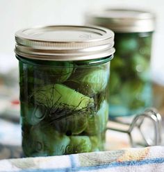 two jars filled with pickles sitting on top of a table next to a pair of scissors