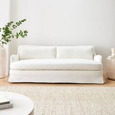 a white couch sitting on top of a wooden floor next to a vase filled with green plants