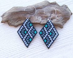 a pair of blue and black beaded earrings sitting on top of a piece of wood